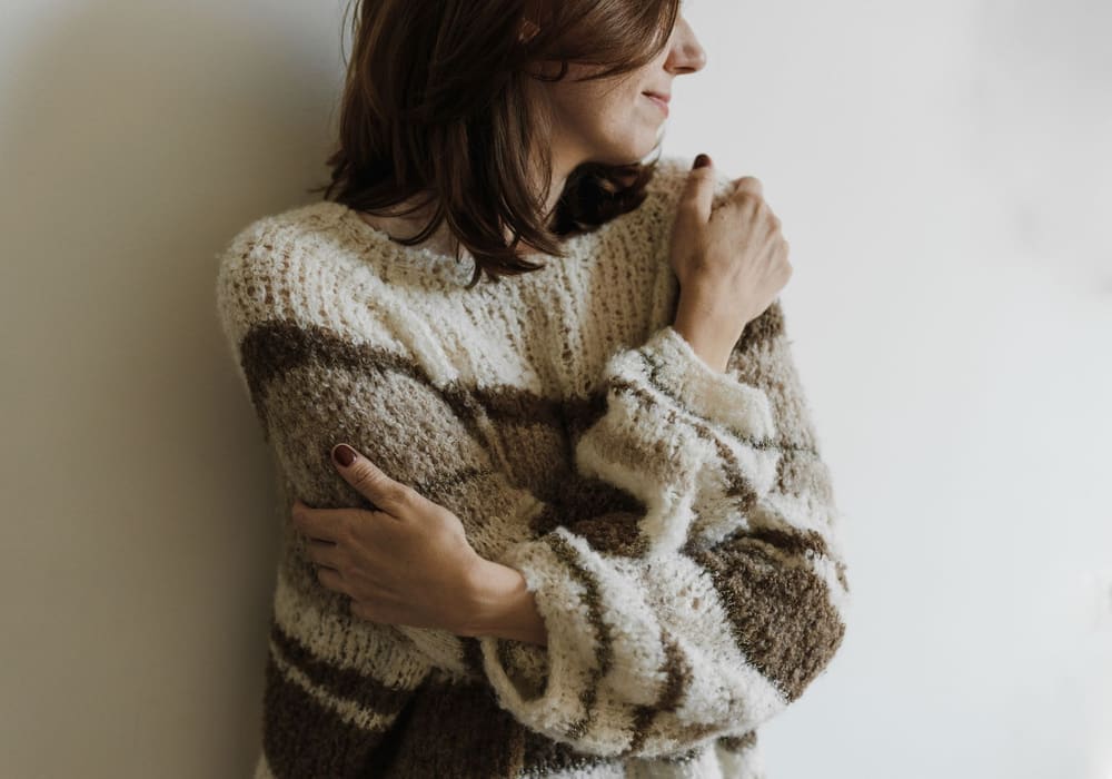 Femme enveloppée dans un pull doux, les bras autour d'elle-même